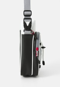 Borsa nera e bianca con una superficie testurizzata, una tracolla grigia, zip rosse e una chiusura distintiva sul lato per una chiusura sicura.
