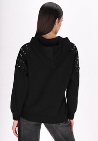 Felpa con cappuccio nera con dettagli a borchie sulle spalle. Realizzata in tessuto morbido, presenta polsini e orlo a costine, con un design a vestibilità rilassata.