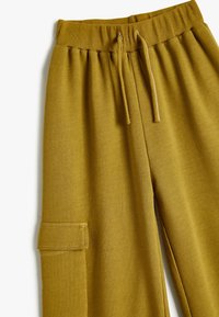 Senfgelbe Sweatpants mit geripptem Bund, Kordelzug und Seitentasche. Hergestellt aus weichem Stoff mit glatter Textur.