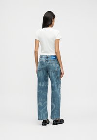 Φωτεινό γαλάζιο τζιν με ίσια γραμμή, ξεθωριασμένα σχέδια, ψηλή μέση με μπλε λογότυπο, συνδυασμένο με λευκό εφαρμοστό μπλουζάκι.