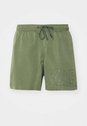 Shorts de bain verts avec une taille élastique, cordon de serrage et un grand graphique "KAR" noir sur la jambe gauche. Texture de tissu lisse.