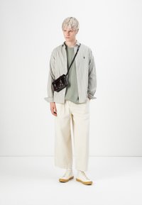 Stripet grå og hvid overskjorte over en grøn sweatshirt, parret med hvide brede bukser og cremefarvede sneakers. Sort crossbody taske båret.