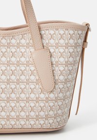 Beige tote bag with a textured fabric featuring a geometric pattern. Smooth leather accents and a single strap with stitching details.