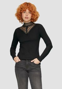 Schwarzes Langarmoberteil mit hohem Kragen, der mit einem dekorativen Spitzen- und geometrischen Muster sowie einem strukturierten Stoff versehen ist.