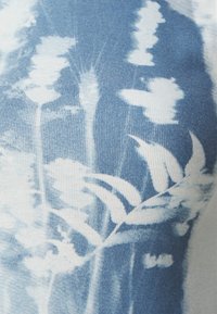 Blått og hvitt mønstrete stoff med ribbet tekstur som har abstrakte blomsterdesign i lysere nyanser.
