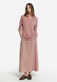 Ljusrosa blus med lång ärm, krage och avslappnad passform, matchad med en lång kjol och bruna sandaler med remmar.