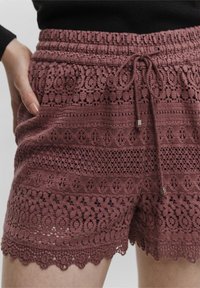 Koronkowe szorty w kolorze przykurzonego różu z fakturowanym wykończeniem. Charakteryzują się elastycznym pasem, sznurkiem do regulacji oraz falbaniastym dołem z misternymi wzorami.