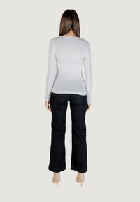 Top blanco de manga larga ajustado combinado con jeans de pierna ancha negros de cintura alta. El modelo lleva zapatos de tacón alto transparentes. Textura simple y suave.