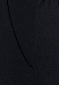 Zwarte stof, met een gestructureerd oppervlak en een lichte glans, met een gebogen naden detail. Het materiaal lijkt zacht en dik, geschikt voor kleding.