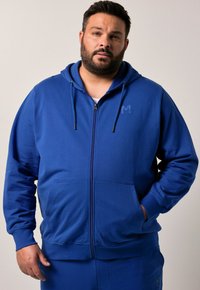 Felpa con zip blu, dotata di cappuccio con cordino, tasche frontali e un logo discreto sul petto, realizzata in tessuto morbido e leggero.