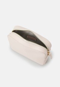 Różowy skórzany kosmetyczny woreczek o teksturowanym wykończeniu, złotym zamku błyskawicznym i brązowej metce wewnątrz. Ma zaokrąglony kształt i zamek błyskawiczny.