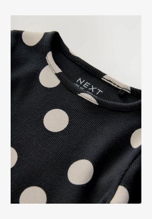 Čierny rebrovaný materiál s veľkými krémovými bodkami. Okrúhly výstrih so švom a viditeľná značková etiketa pri golieri.