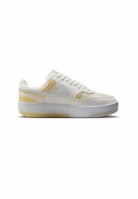 Zapatilla deportiva blanca con detalles en beige, materiales de malla y cuero, puntera redondeada, suela plana y perforaciones en los lados.