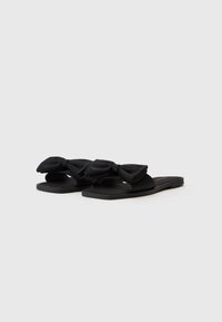 Sandale negre plate cu un superior din material neted, decorate cu două funde mari, cu o talpă simplă și un design cu vârful deschis.