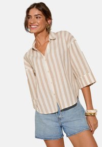 Chemise boutonnée avec rayures verticales beige et crème, design à col, coupe ample, manches trois-quarts, associée à un short en denim clair.