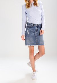 Farkkuhame, jossa on repsottava helma, vaaleansininen pesu ja näkyvät kulumat. Yhdistetty pitkään hihaiseen vaaleanpunaiseen yläosaan ja valkoisiin lenkkareihin.