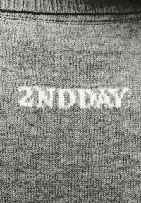 Γκρι πλεκτό ύφασμα με λευκό κείμενο πλεκτό μέσ α, που γράφει «2NT DIDN'T» με μια στιλιζαρισμένη γραμματοσειρά.