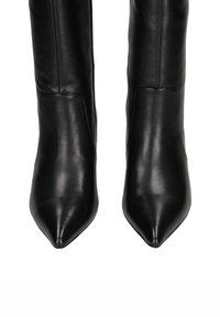 Bottes en cuir noir montantes avec un embout pointu, texture lisse et coutures minimales, dotées d'une fermeture à glissière sur le côté intérieur.