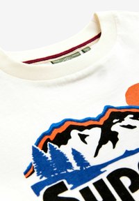 Cremefarvet bomulds t-shirt med et grafik af blå bjerge, grønne træer og en orange sol. Udhalsen er ribbede.
