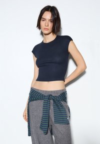 Tmavě modrý krátký přiléhavý top s krátkými rukávy, doplněný o šedé vysoké tepláky zdobené zeleně pruhovanou stuhou v pase.