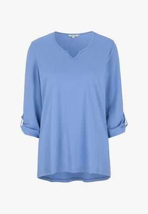 Lichtblauwe, langslavige top van zachte stof, met een V-hals, omgeslagen manchetten vastgezet met knopen, en een iets langere achterzoom.