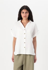 Blusa bianca a maniche corte con chiusura a bottoni sul davanti, leggero lucido, e maniche arrotolate; il tessuto sembra leggero e liscio.
