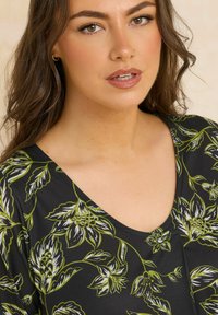 Indumento nero con scollatura a V caratterizzato da un motivo floreale in bianco e verde. Texture liscia con un design aderente.