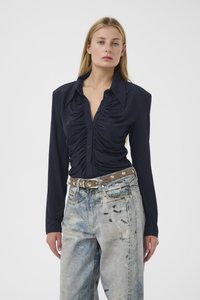 Marineblauw aansluitend overhemd met knoopsluiting en geplooide details aan de voorkant, gecombineerd met lichtgewassen wijd uitlopende jeans met scheuren en een gespikkelde riem.