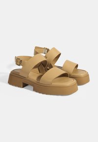 Beige Leder-Sandalen mit Kreuzriemen und Schnallenverschluss, die eine klobige Plateausohle mit Zickzackmuster aufweisen.