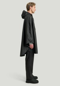 Svart huva regnponcho tillverkad av vattentätt material, med lös passform och långa ärmar, i kombination med matchande svarta byxor och skor.