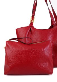 Bolso tote de cuero rojo con textura arrugada y un acento de hardware dorado. Incluye un estuche con cremallera a juego con una manija.