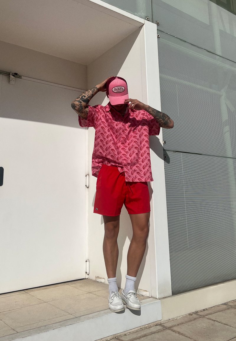 Roze patroon overhemd met korte mouwen, rode shorts, witte sneakers en een roze pet. Gecombineerde look met levendige kleuren en een casual zomerstijl.