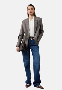 Rutet blazer i brune nuancer, hvid polo med knapper, højhalsede blå jeans, brun taske og spidse brune sko.