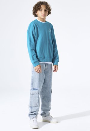 Turquoise sweatshirt met geribbelde manchetten, gecombineerd met lichtblauwe cargobroek met zijzakken en witte sneakers. Minimalistisch ontwerp.