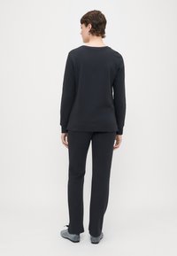 Sudadera negra y pantalones a juego de tejido suave; la sudadera tiene un escote redondo y mangas largas, y los pantalones tienen un corte recto.