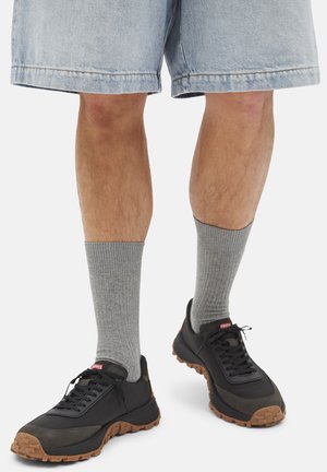 Legs wearing light denim shorts, gray ribbed socks, and black sneakers with brown soles on a white background.