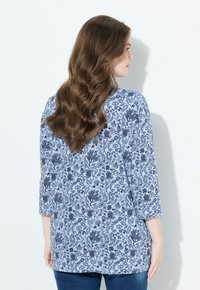 Světle modrá tunika s květinovým vzorem v námořnické modři, tři čtvrtinové rukávy a volný střih. Hladká textura, ležérní design.
