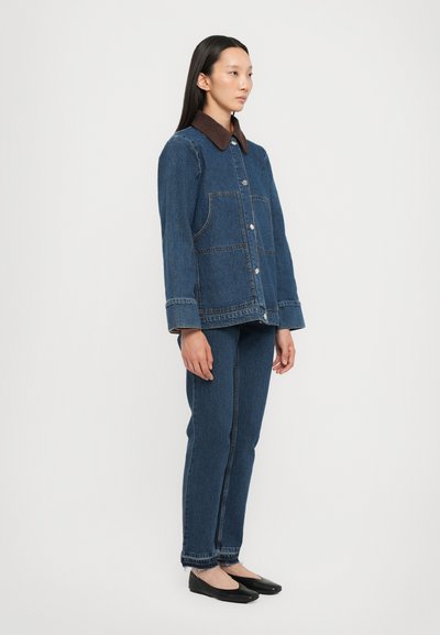 Jeans jakna z rjavim žametnim ovratnikom, dvema sprednjima žepoma in zapiranjem na gumbe. Ujemajoče se modre jeans hlače in črne balerinke.