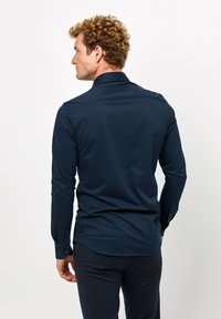 Camicia a maniche lunghe blu navy con colletto classico, polsini con bottone e una texture morbida e liscia. Fit su misura con orlo curvo.