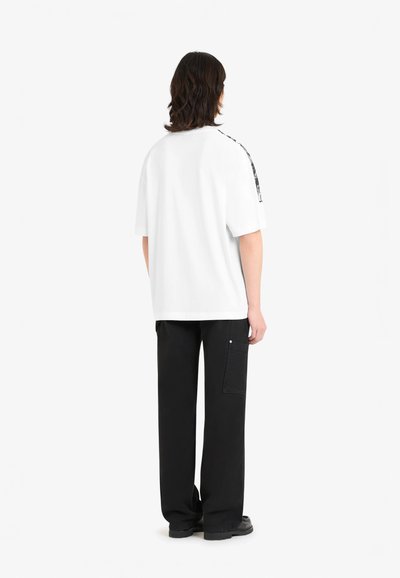 T-shirt blanc à manches courtes avec une coupe ample, présentant un accent texturé noir en motif le long des épaules et un pantalon large noir.