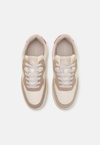 Sneakers Calvin Klein cu piele bej și accente din suede maro deschis, prezentând șireturi albe și un tab pentru călcâi roșu. Talpă plată, design minimalist.