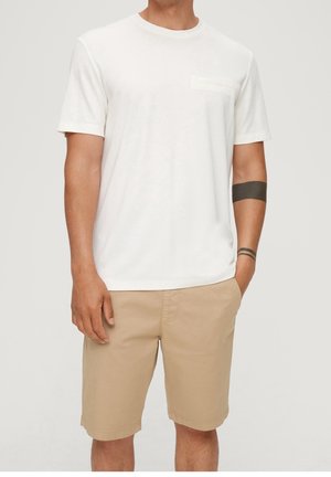 T-shirt en coton blanc avec un col rond et des manches courtes, présentant une petite poche ; associé à un short beige. Texture lisse, coupe décontractée.