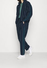 Marinblå randig träningsdräkt med en zip-up-jacka och matchande byxor med teal-accenter. Buren med vita sneakers, vilket ger en avslappnad passform.