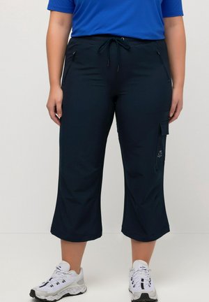 Person wearing navy cropped cargo pants with front and side pockets, paired with white athletic shoes and a blue top.