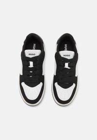 Baskets noires et blanches avec un design épuré, fermeture à lacets, bout perforé et logo de la marque sur la languette.