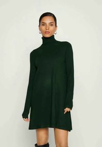 Mørkegrønn turtleneck-kjole med lange ermer, løs passform og glatt tekstur. Den går til over kneet, med subtile sideslit.