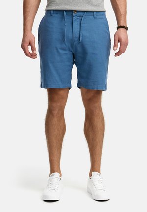 Pantaloni corti in lino blu con vita elastica e cordoncino. Presentano tasche laterali e chiusura con bottone, abbinati a sneaker bianche.