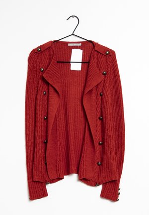 Czerwony sweter na drutach z długimi rękawami, ozdobnymi guzikami z przodu, na ramionach i mankietach, wiszący na czarnym wieszaku z białą metką.