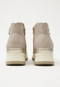 Un par de botas de ante beige hasta el tobillo con cremalleras laterales y suelas de goma texturizadas, vistas desde la parte trasera sobre un fondo blanco.