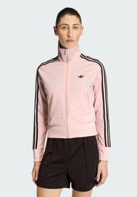 Ružová tréningová bunda so zipsom, �čierne pruhy na rukávoch a malým čiernym logom na hrudi. Vyrobená z hladkej, ľahkej látky.